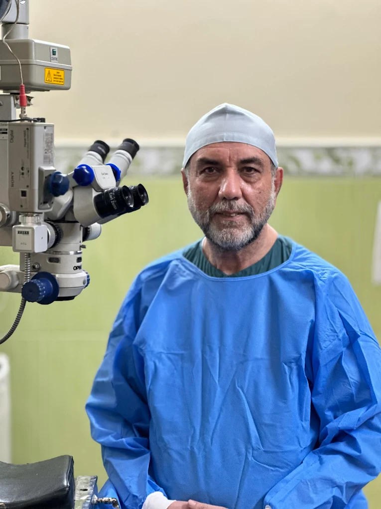 Dr. Nusrat Ullah Khan in surgical attire beside a Zeiss ophthalmic surgical microscope